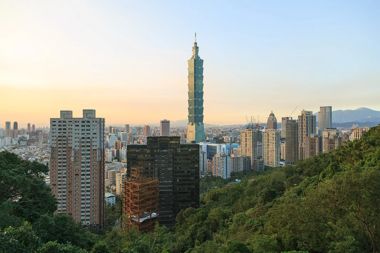 Taipei 101 sobre edificios urbanos y una ladera verde al atardecer