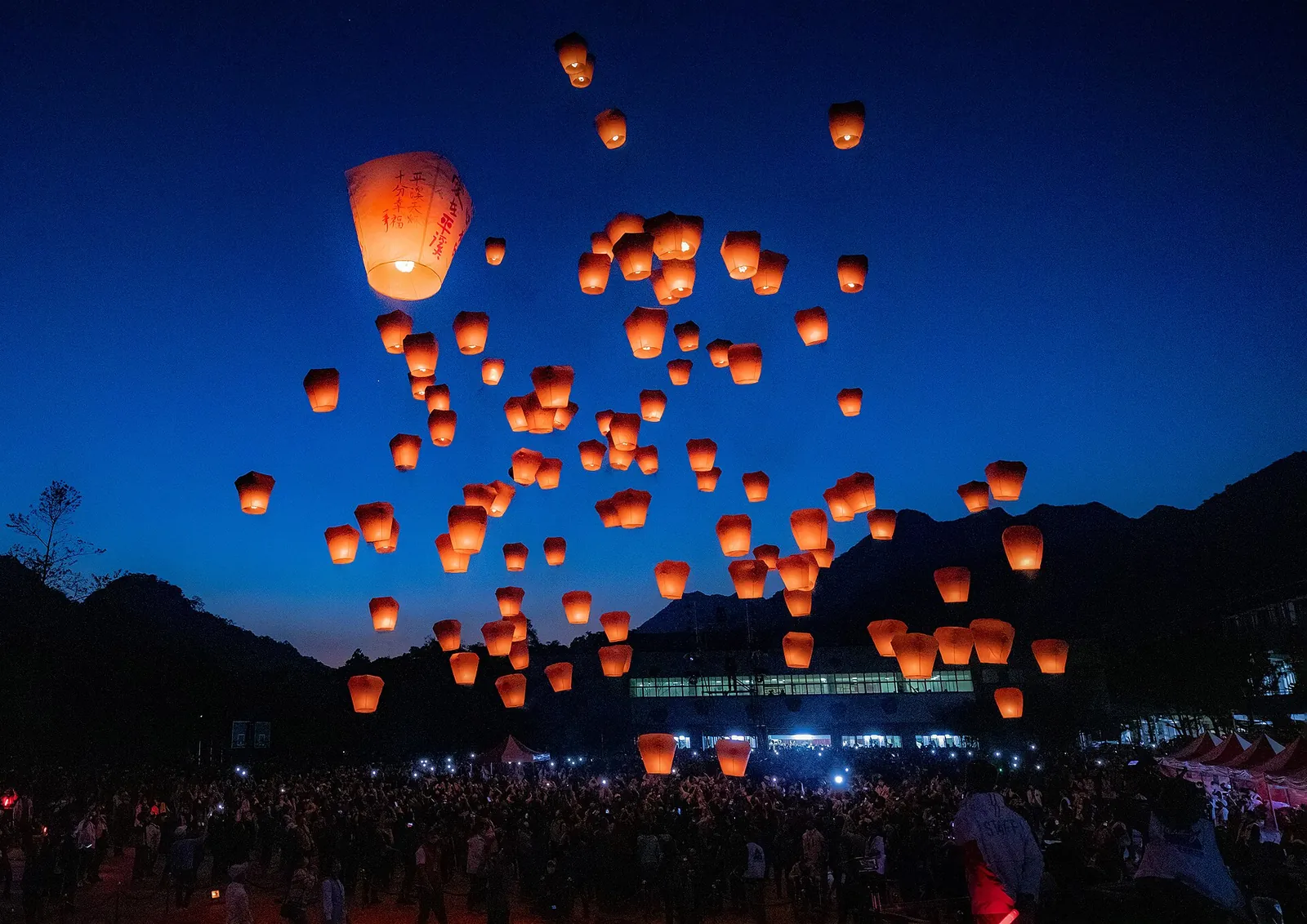 Setki świecących latających lampionów wznoszą się nad tłumem i wzgórzami o zmierzchu w Pingxi
