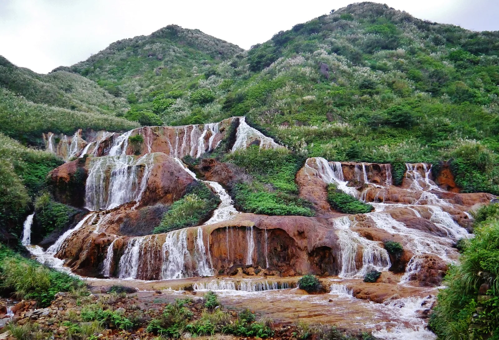 Golden Waterfall stékající po oranžovohnědých skalách u Jinguashi