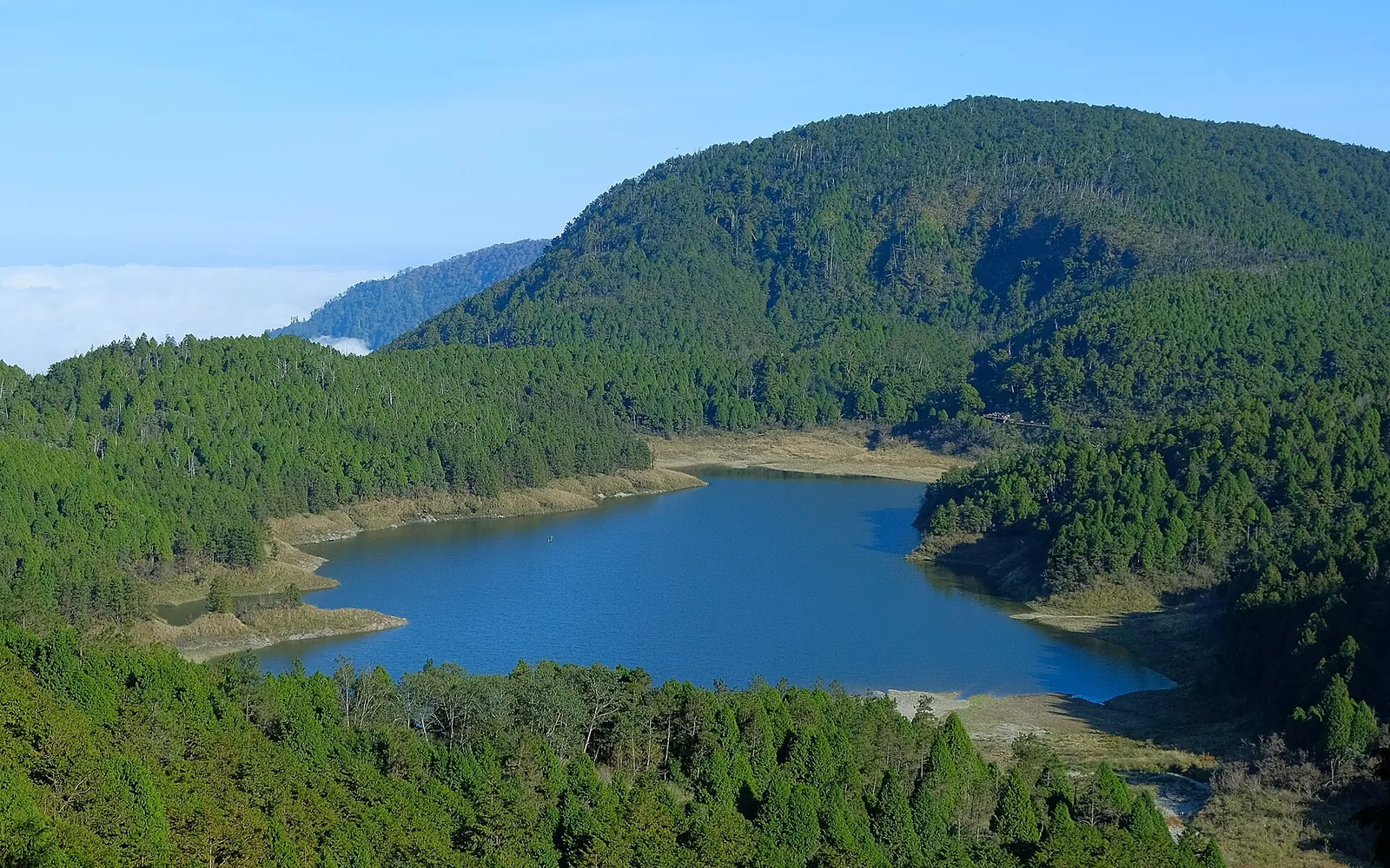 Jezero Cueifong obklopené lesem pod modrou oblohou