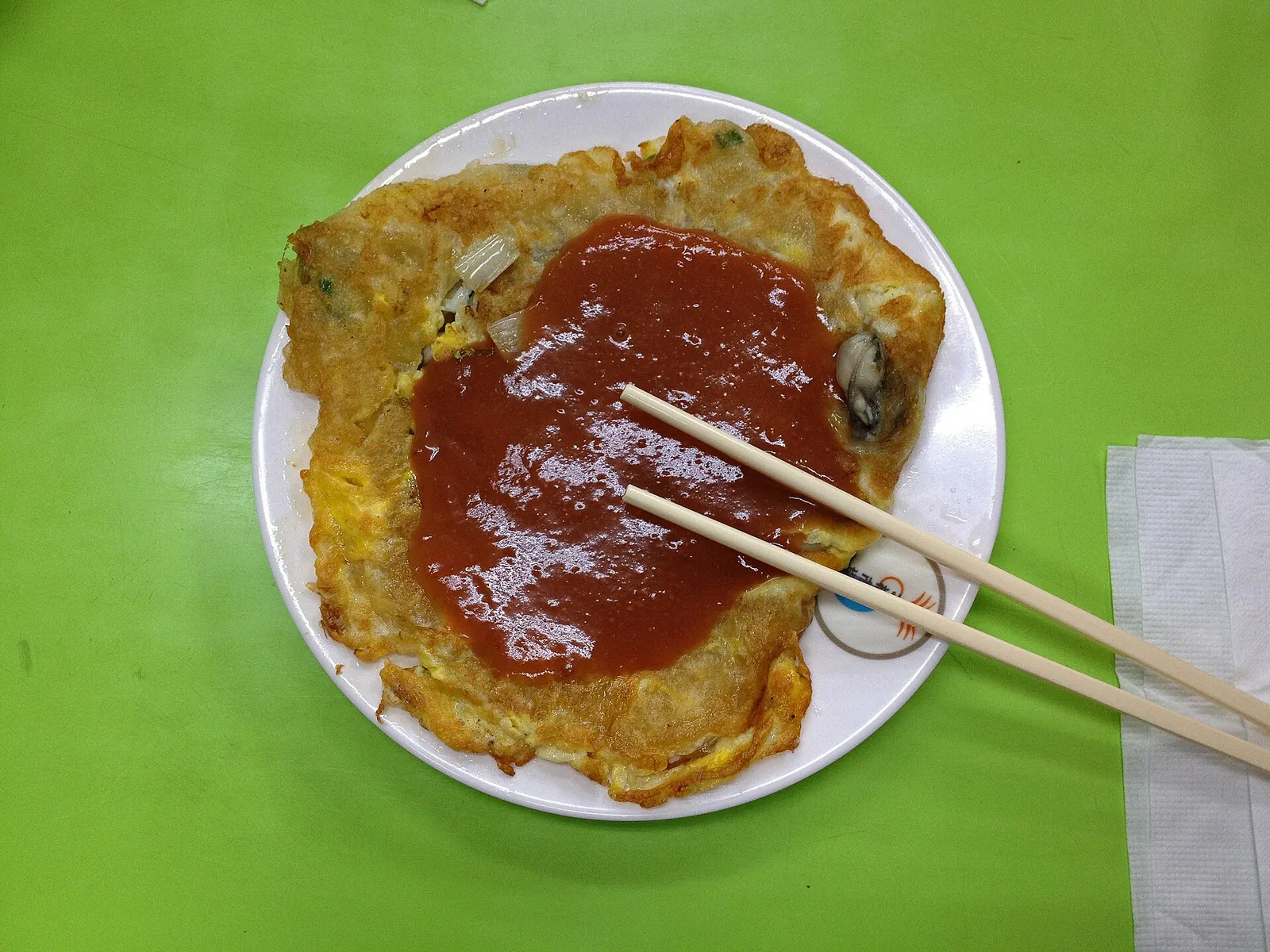 Ústřicová omeleta s omáčkou a hůlkami na stole v Taipei