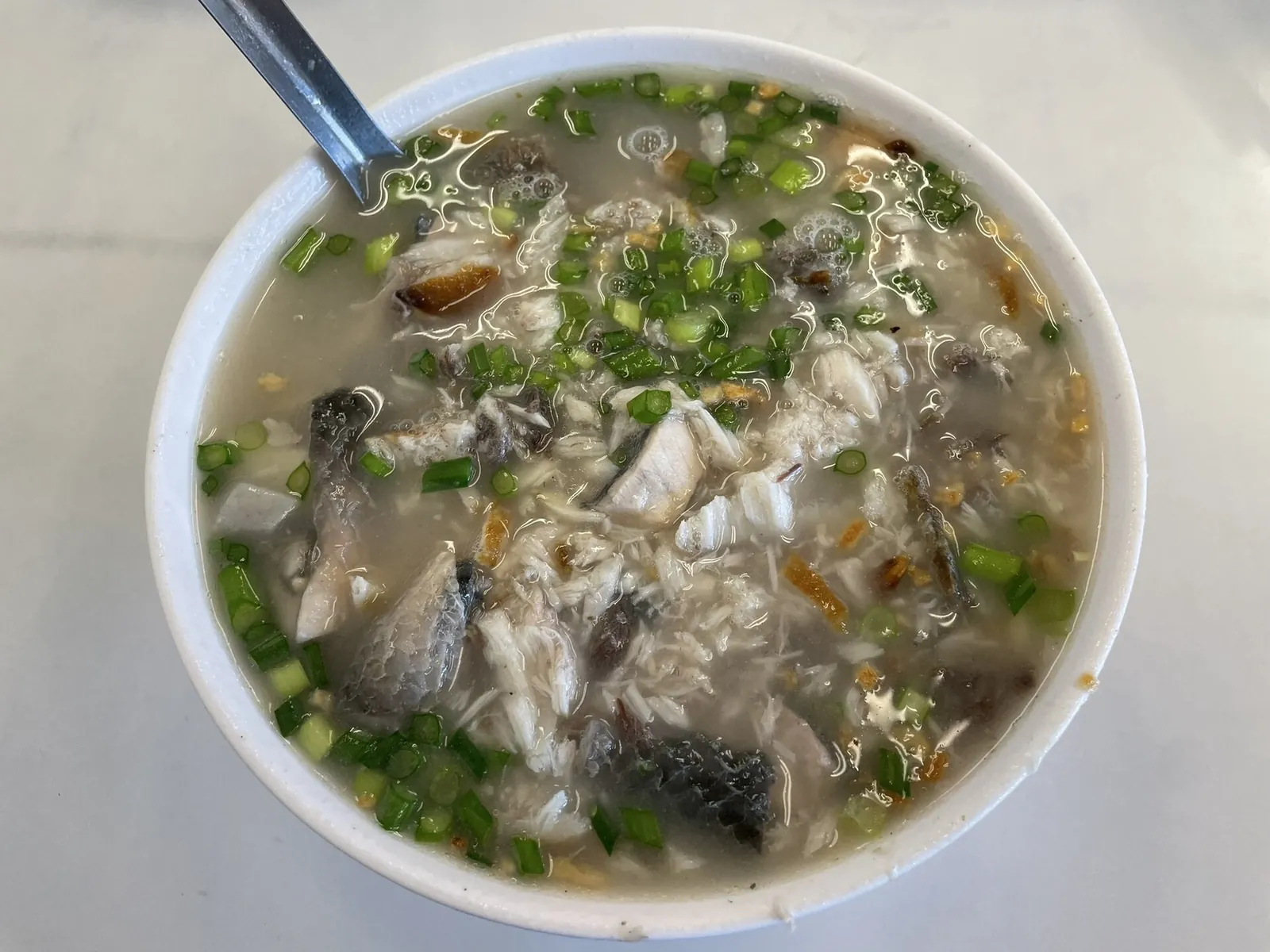 Kaše s rybou milkfish a nasekanou zelenou natí v bílé misce