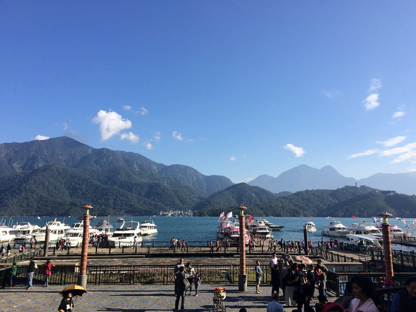 Boats at Shuishe pier on Sun Moon Lake with green mountains under a blue sky