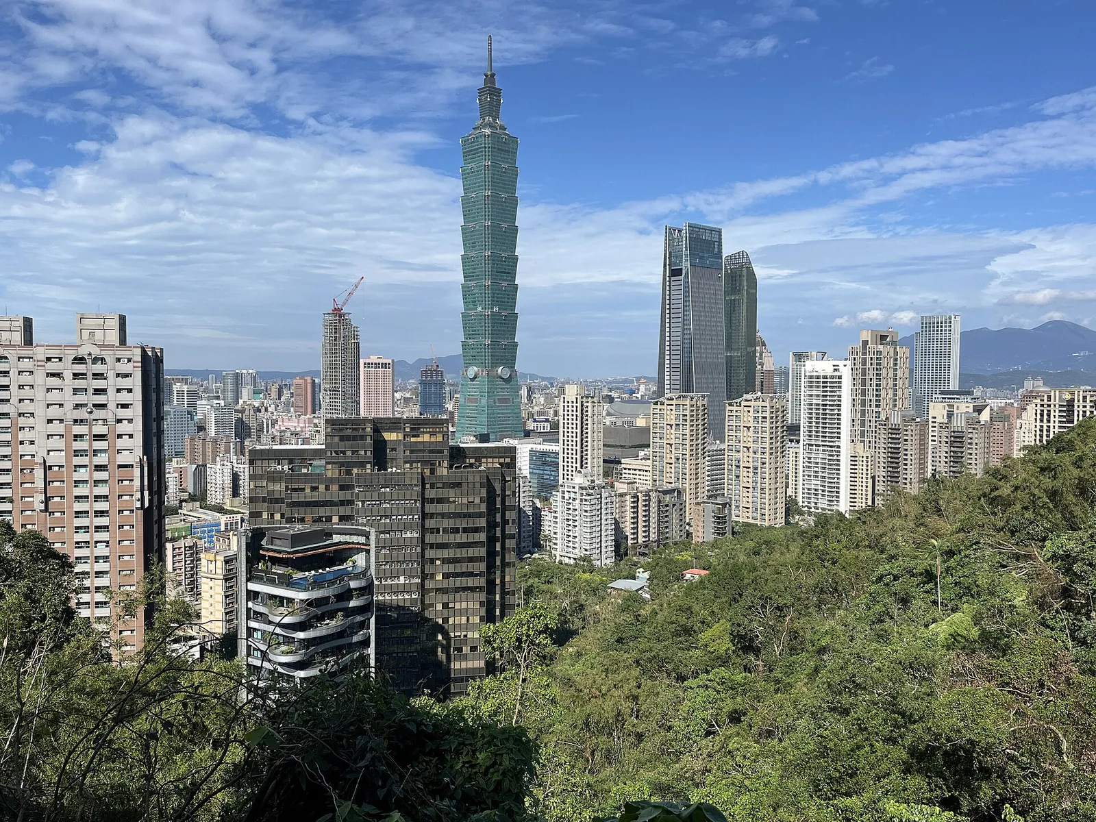 Taipei 101 rising above the city behind green hillside trees