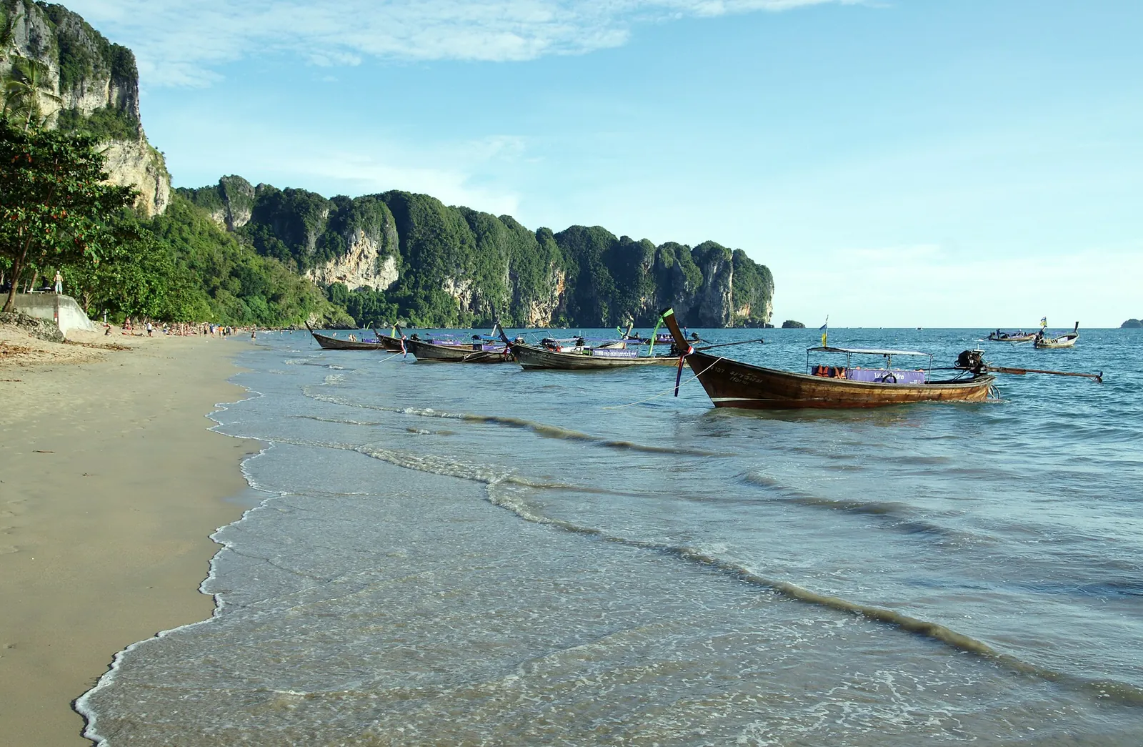 Barche a coda lunga sull'acqua accanto alla spiaggia di Ao Nang e alle scogliere calcaree