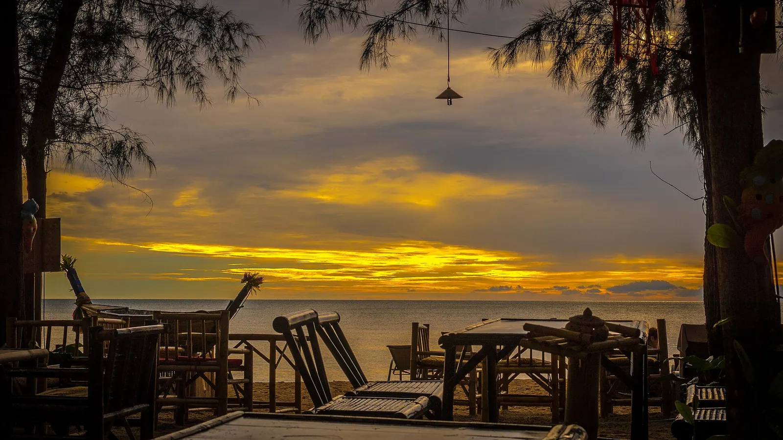 Tavoli e sedie stagliati sotto un tramonto dorato su Koh Lanta