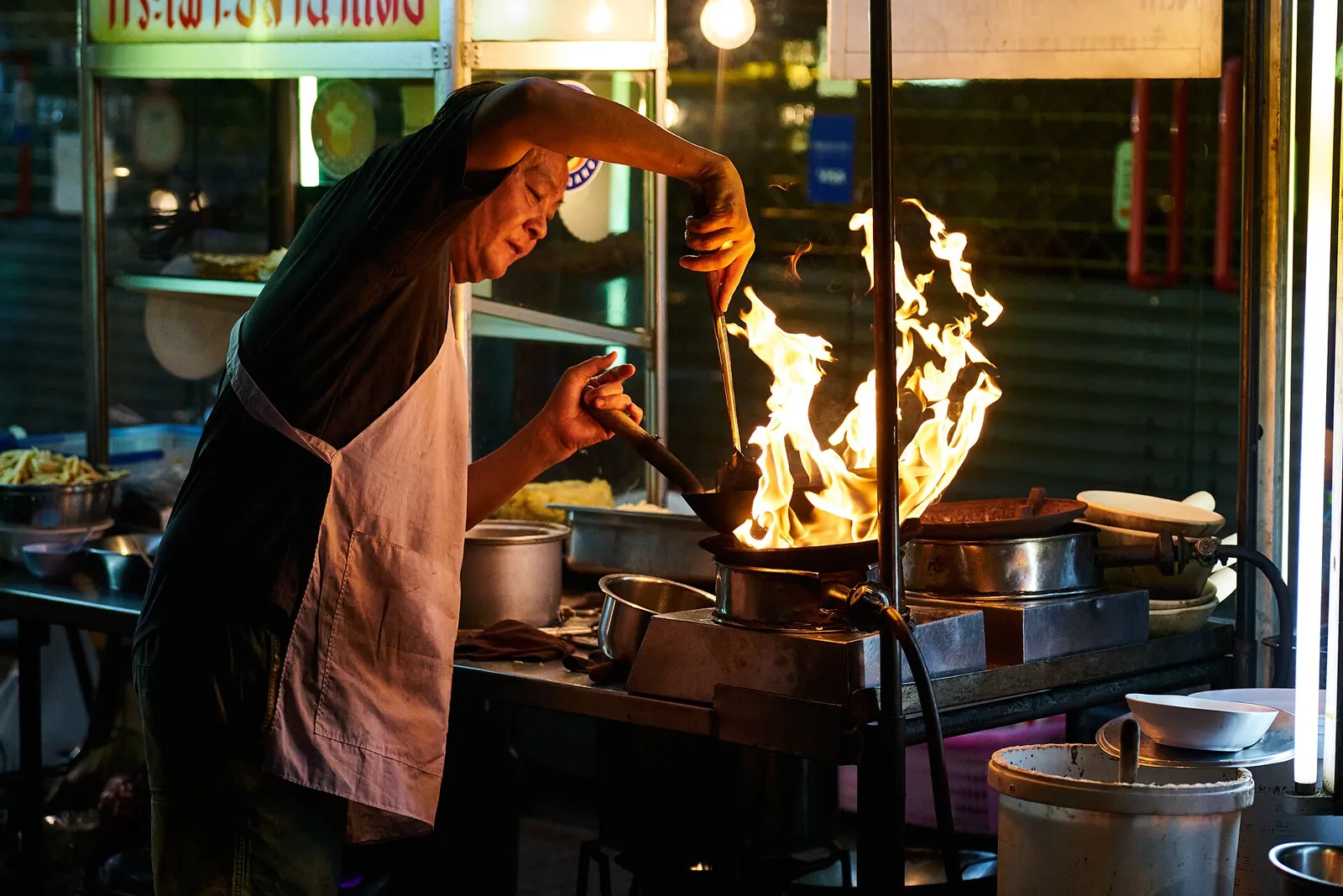 En gatekokk svinger en wok over høy flamme ved en matbod i Chinatown i Bangkok