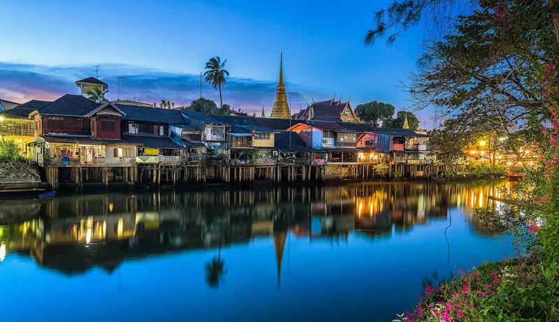Old wooden houses of the Chanthaboon waterfront lit at dusk and reflected in the river