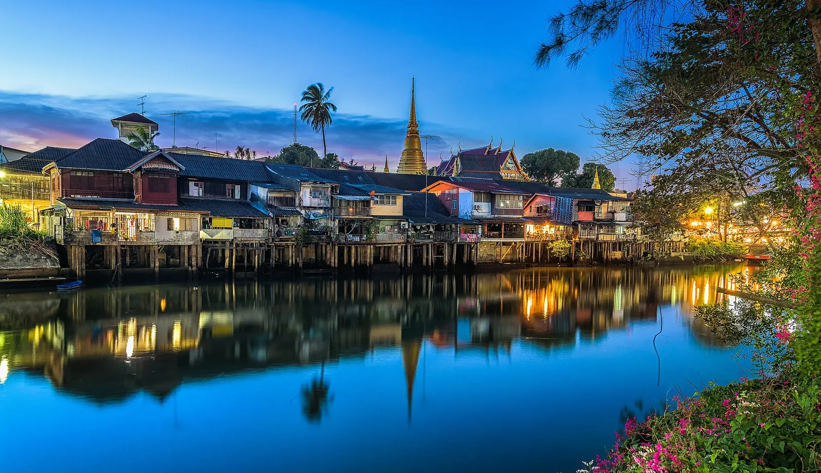 Old wooden houses of the Chanthaboon waterfront lit at dusk and reflected in the river