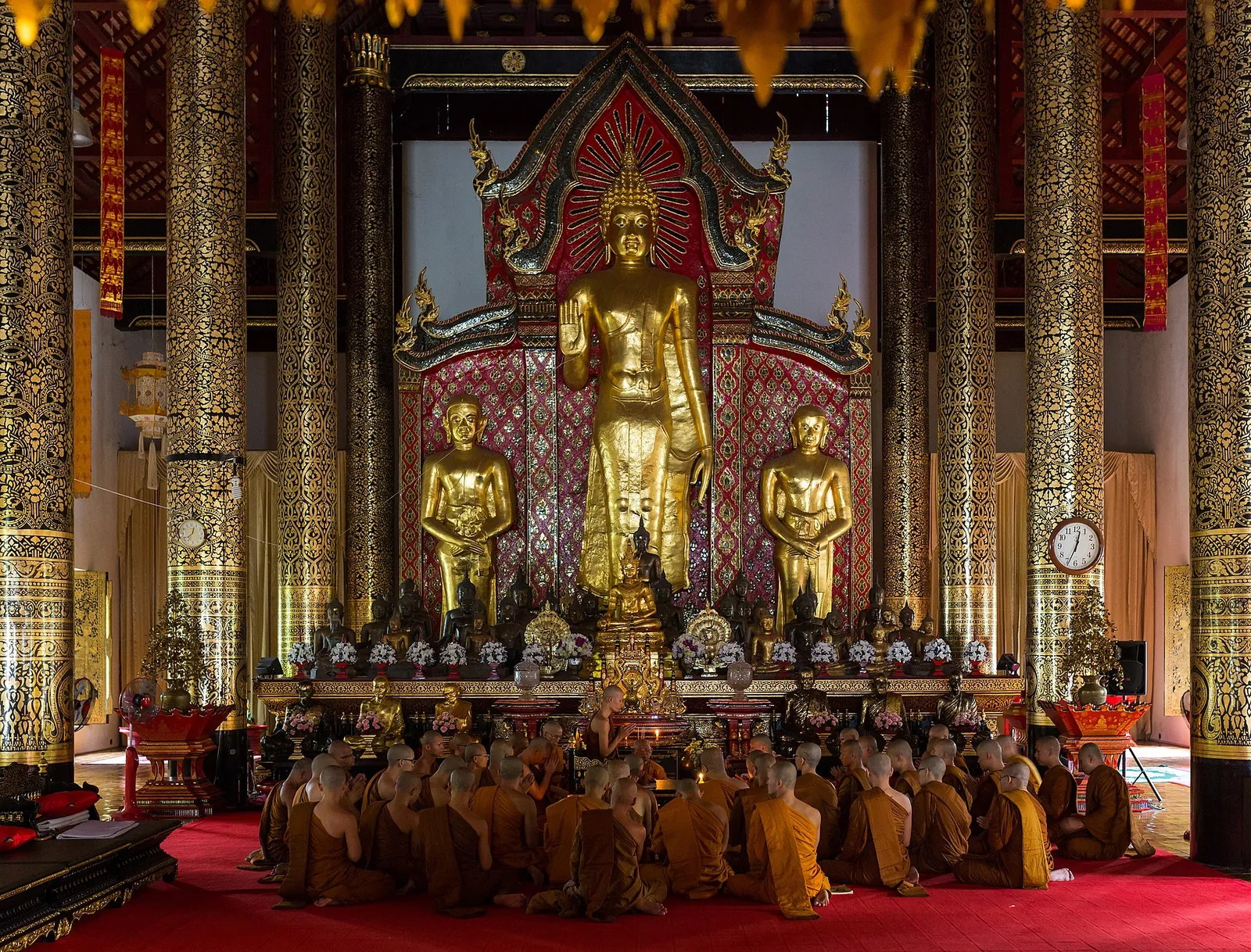 Monjes sentados debajo de imágenes doradas de Buda dentro del salón de actos de Wat Chedi Luang en Chiang Mai.