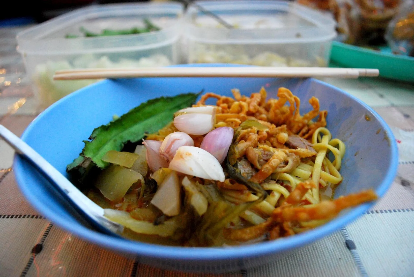 Khao soi en un bol azul con fideos crujientes, pollo, chalotes y lima