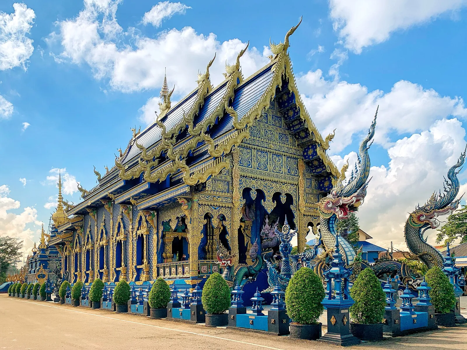 The blue and gold hall of Wat Rong Suea Ten with naga serpents at the entrance