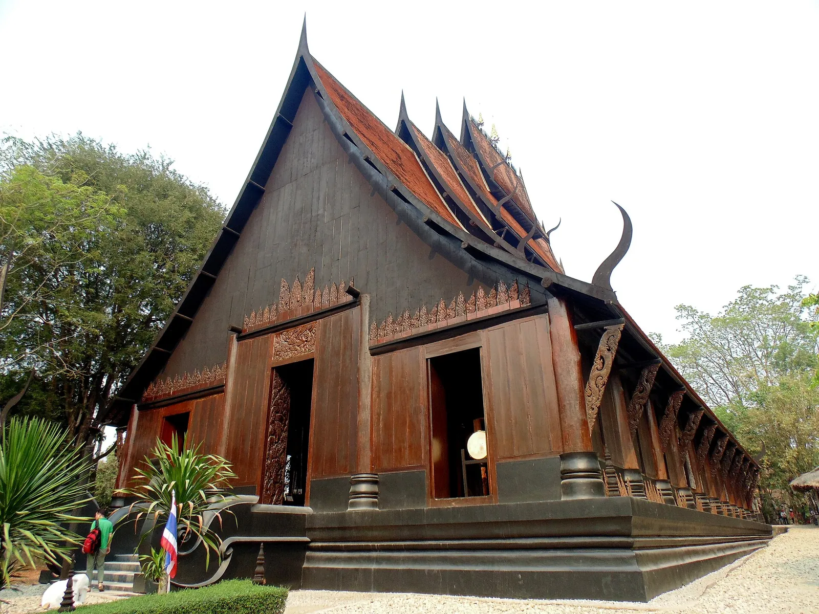 A dark wooden Lanna-style hall with steep layered roofs at Baan Dam