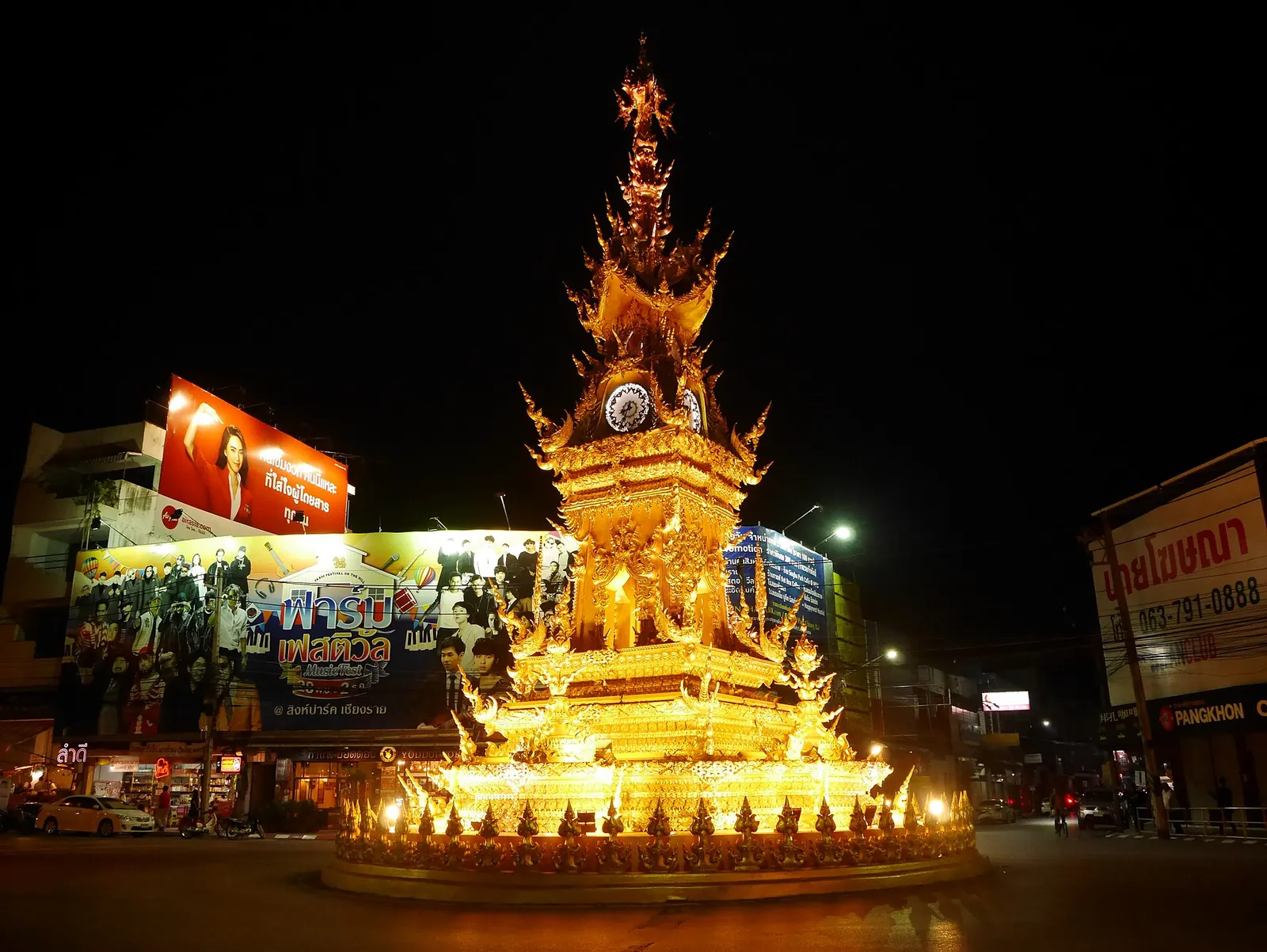 Chiang Rai's golden clock tower lit up at night at a road junction