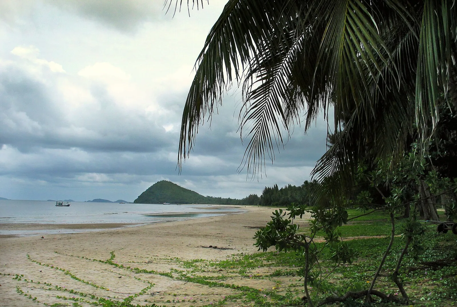 The long sweep of Thung Wua Laen beach with palms and a headland under a cloudy sky