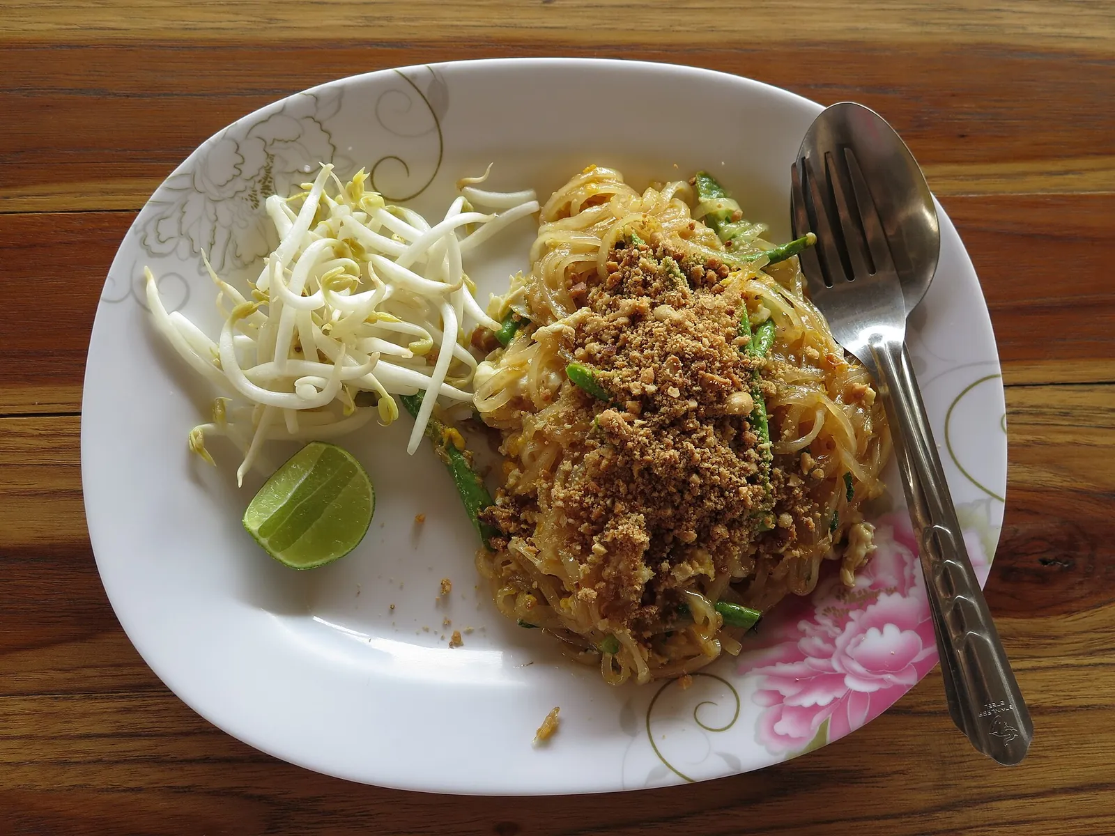 Pad thai s klíčky a limetkou na bílé plotně v Thajsku