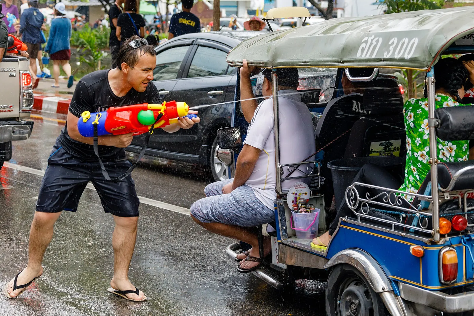 Muž s vodní pistolí kropí tuk-tuk projíždějící mokrou ulicí v Chiang Mai během Songkranu
