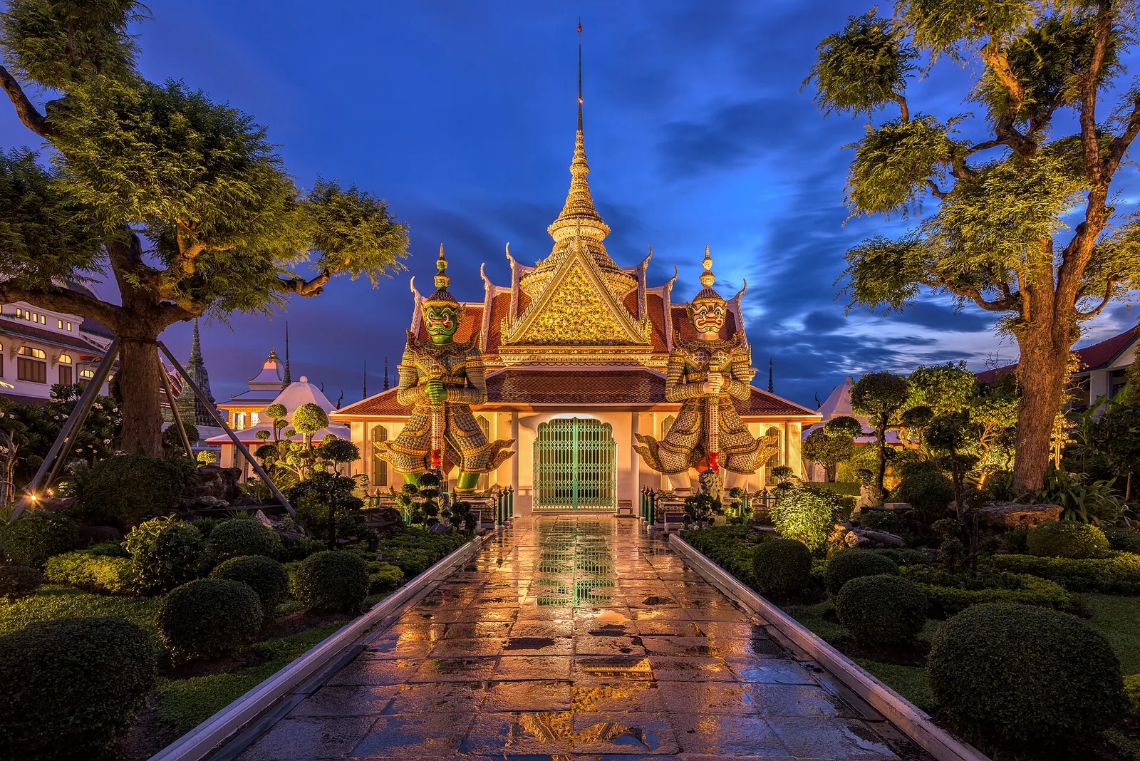 Východní brána Wat Arun a postavy strážců osvětlené proti modré večerní obloze