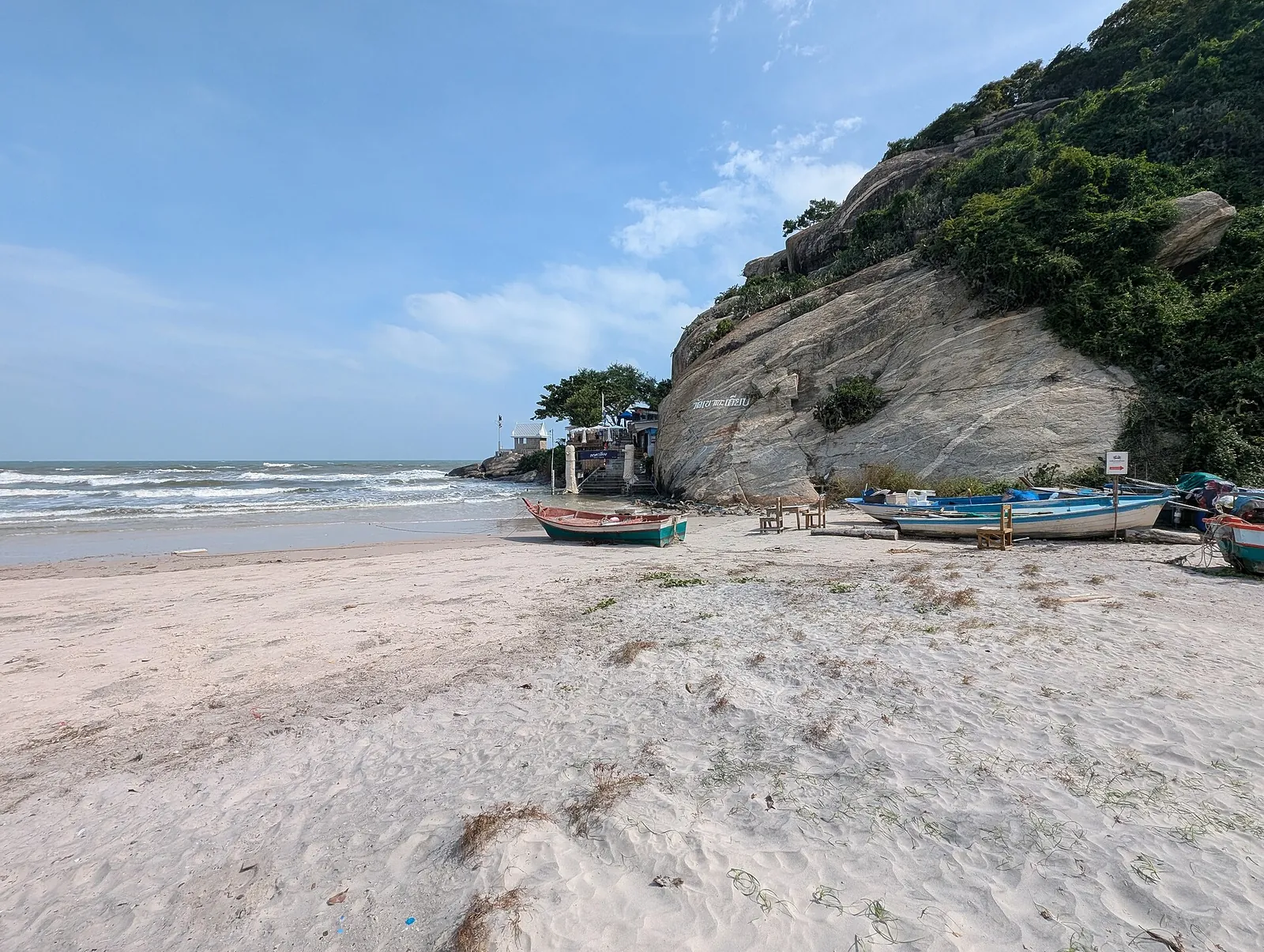 Fishing boats pulled up on white sand beside a rocky headland on Hua Hin beach