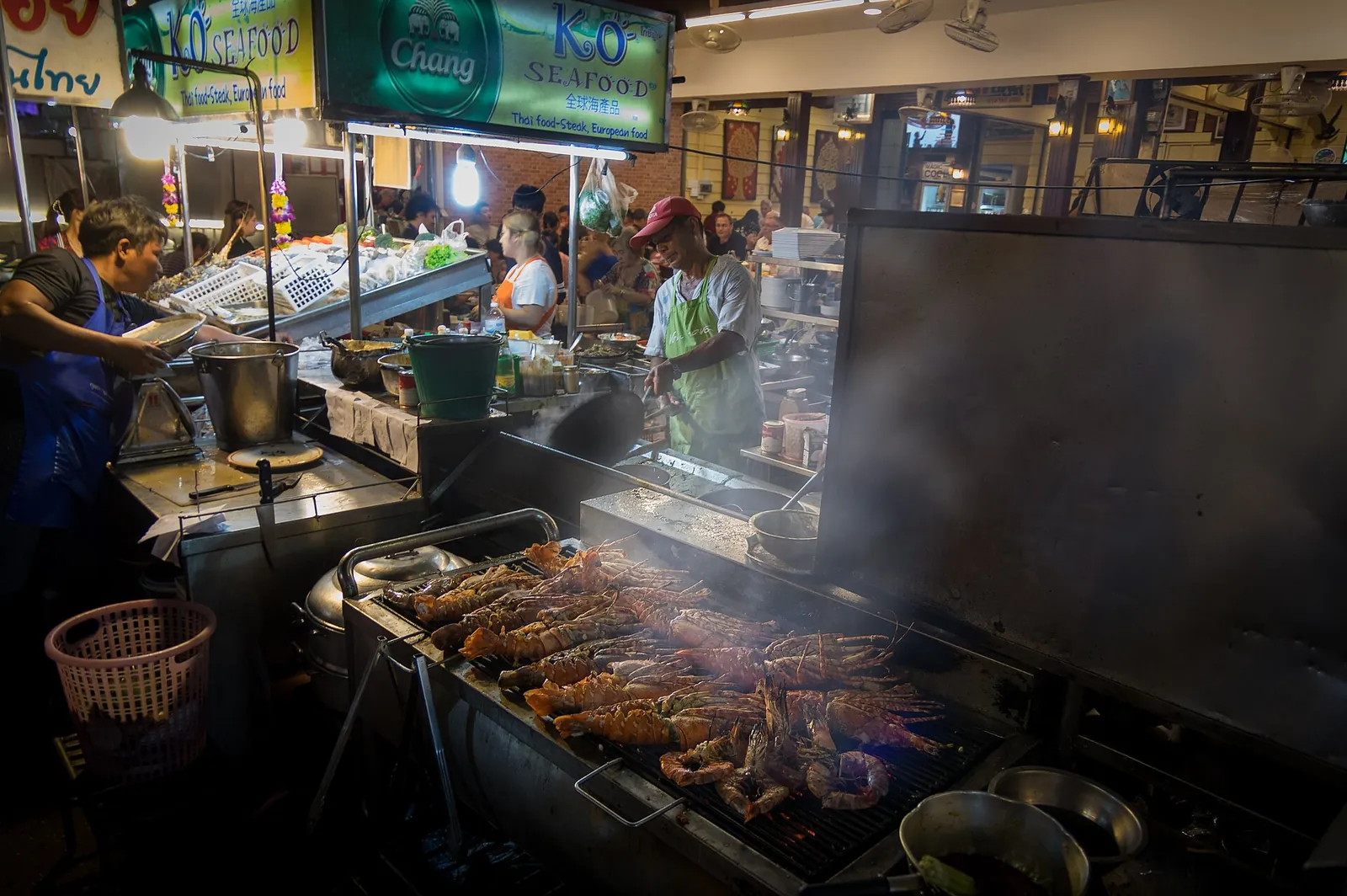 Lobsters and prawns grilling on a large griddle at a night-market seafood stall