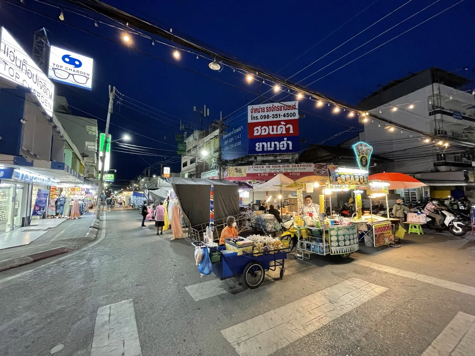 Food stalls under strings of lights along the street of Hua Hin Night Market at dusk