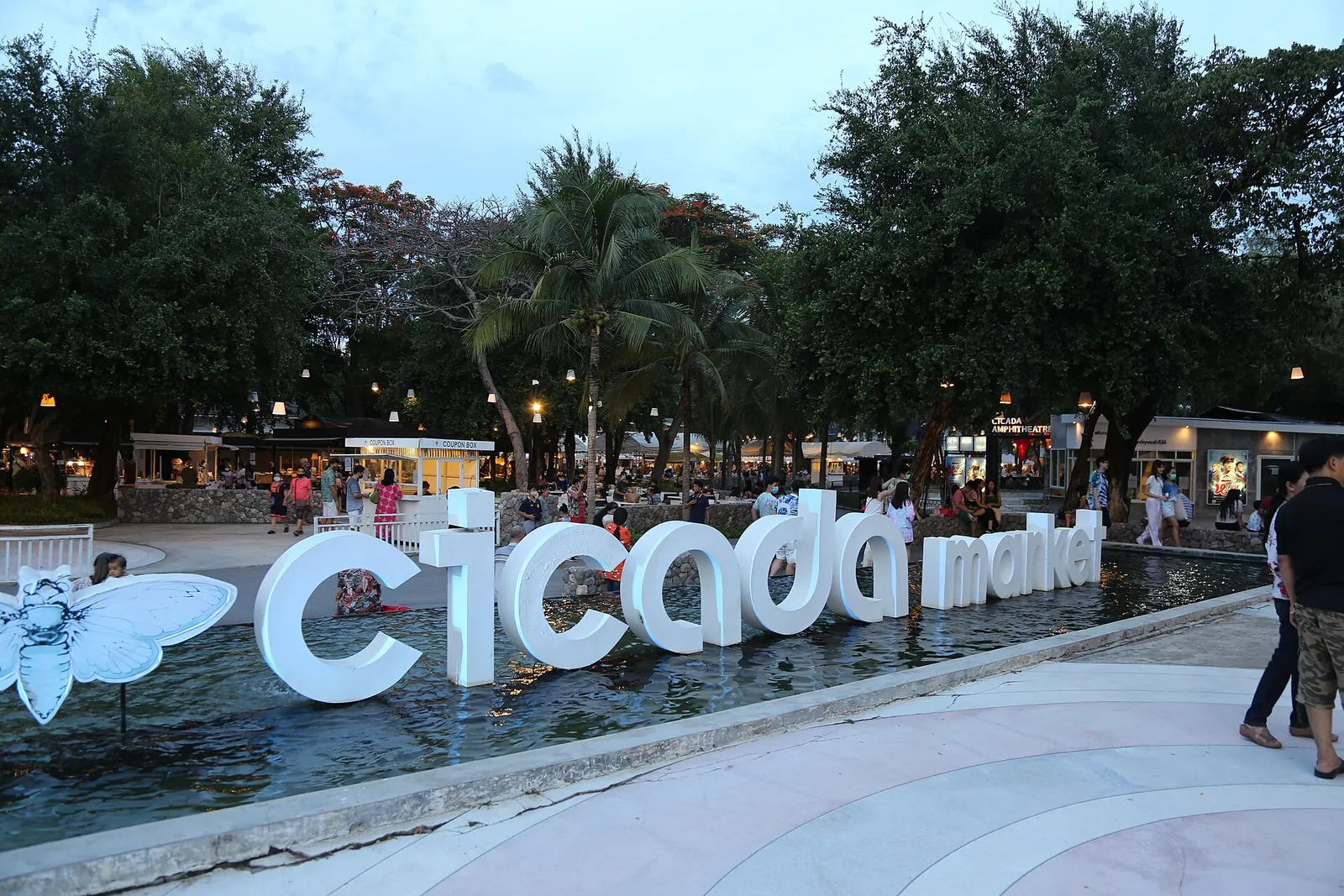 The Cicada Market sign beside a pond in a garden in the early evening