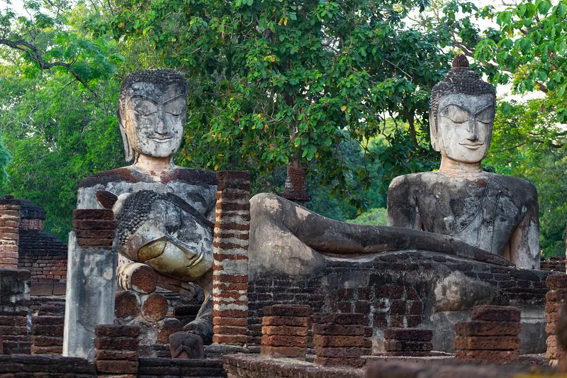 Weathered laterite Buddha images, seated and reclining, among brick ruins and trees