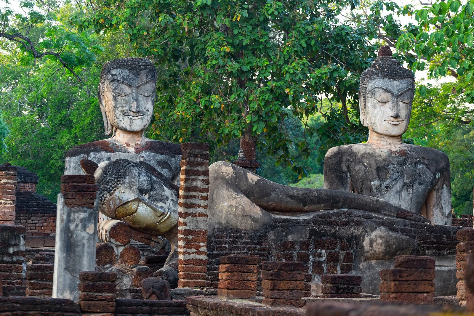 Weathered laterite Buddha images, seated and reclining, among brick ruins and trees