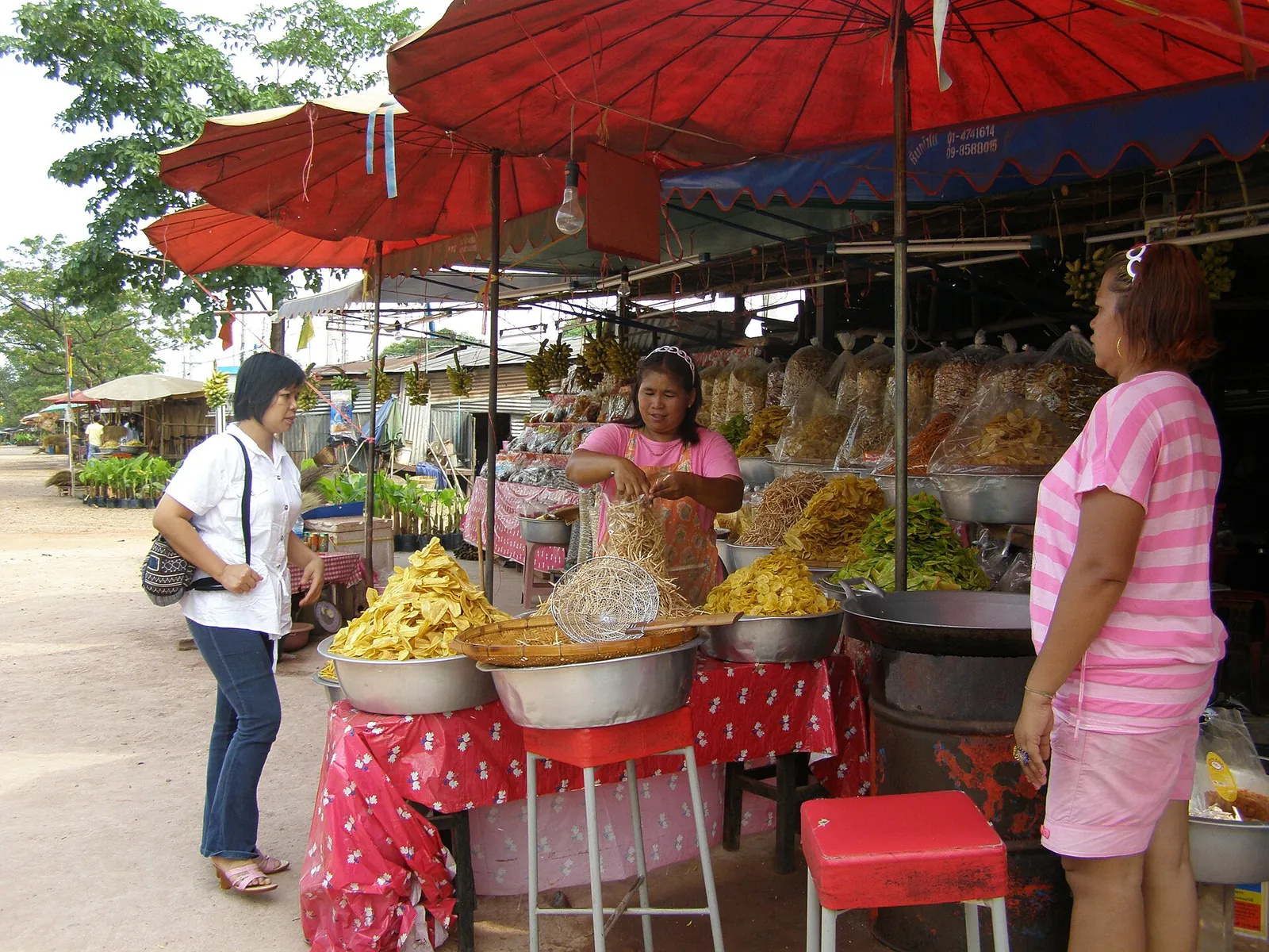 A roadside stall piled with bananas and snacks under red umbrellas in Kamphaeng Phet