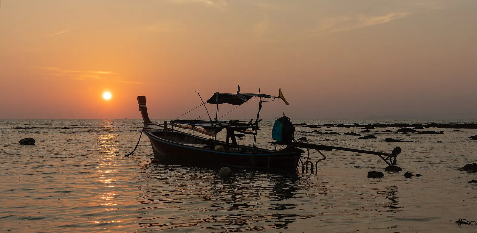 A longtail boat silhouetted against the setting sun at Klong Khong beach