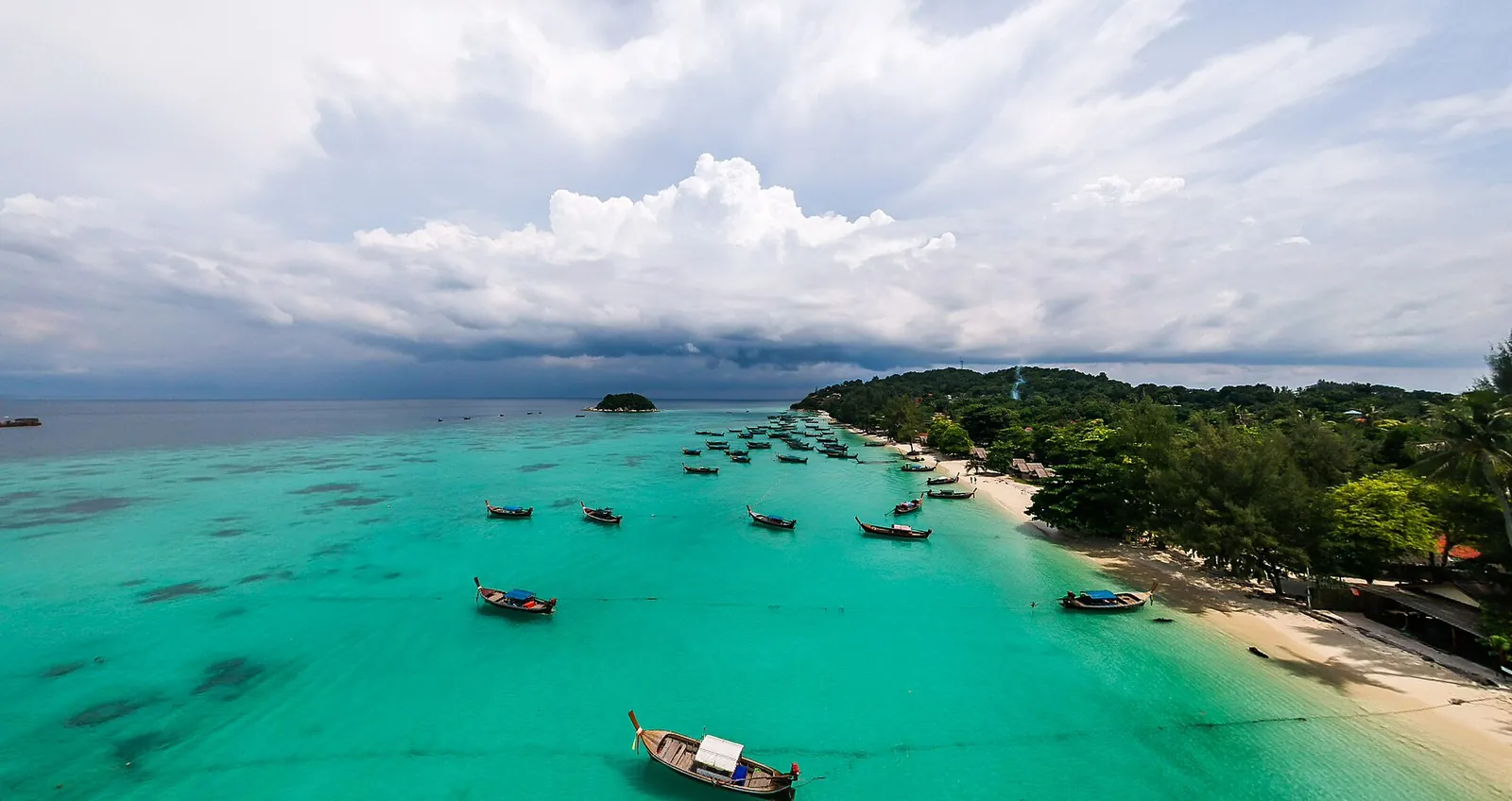 Longtail boats moored in turquoise water along a beach on Koh Lipe seen from above