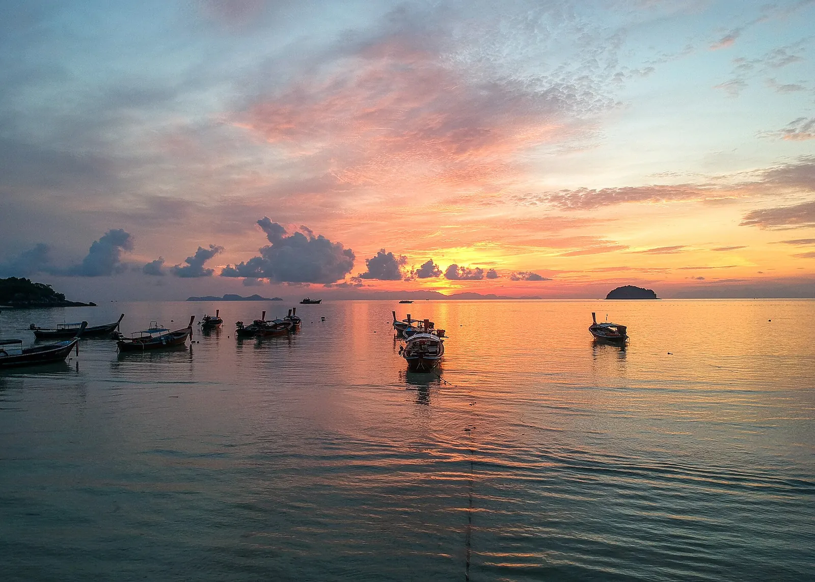 Longtail boats silhouetted against a pink sunrise off Koh Lipe