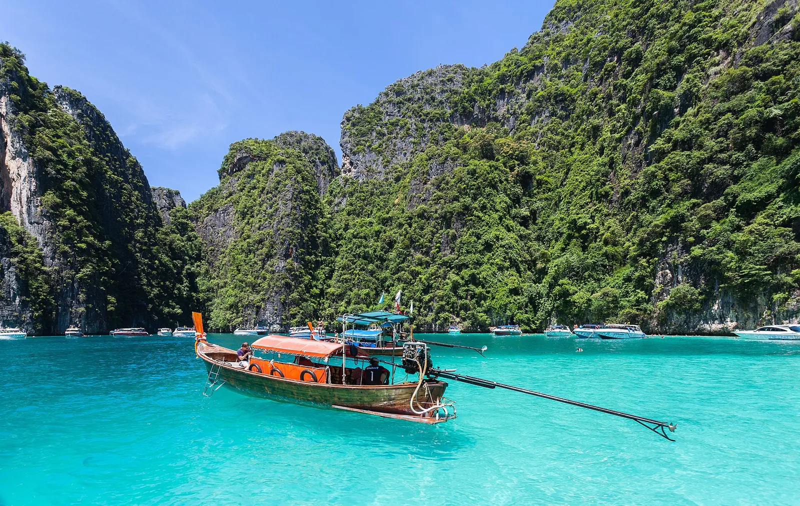 A longtail boat on brilliant turquoise water below forested limestone cliffs at Phi Phi Leh