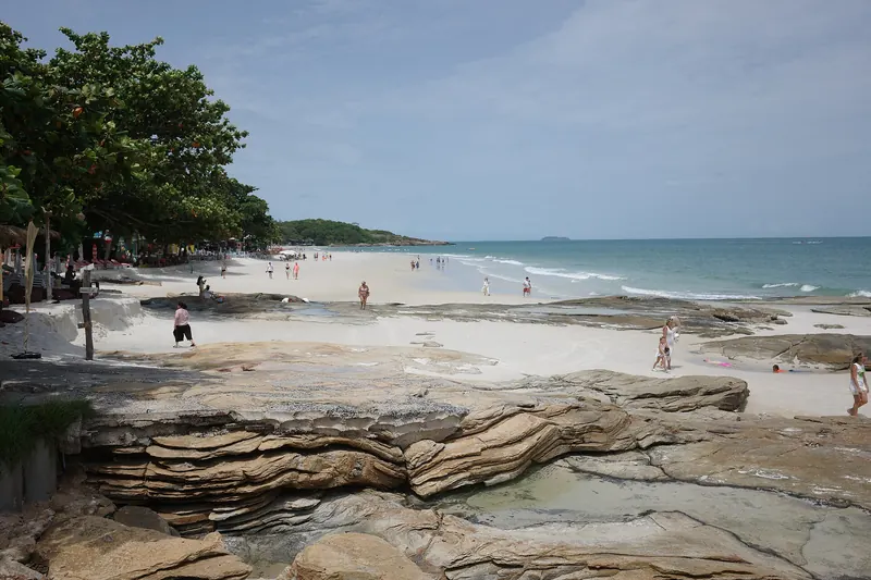 Sandstone ledges and white sand along a Koh Samet beach on a sunny day