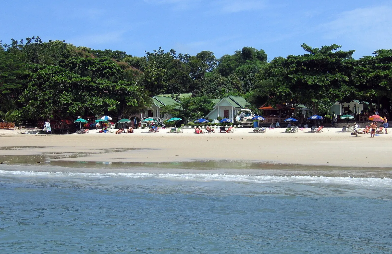 Beach umbrellas and bungalows under trees along the bay of Ao Phai