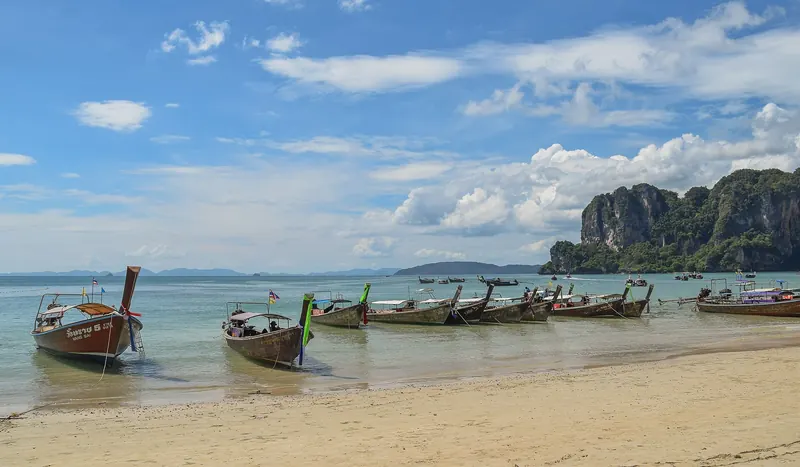 Longtail boats pulled up on West Railay beach below towering limestone cliffs