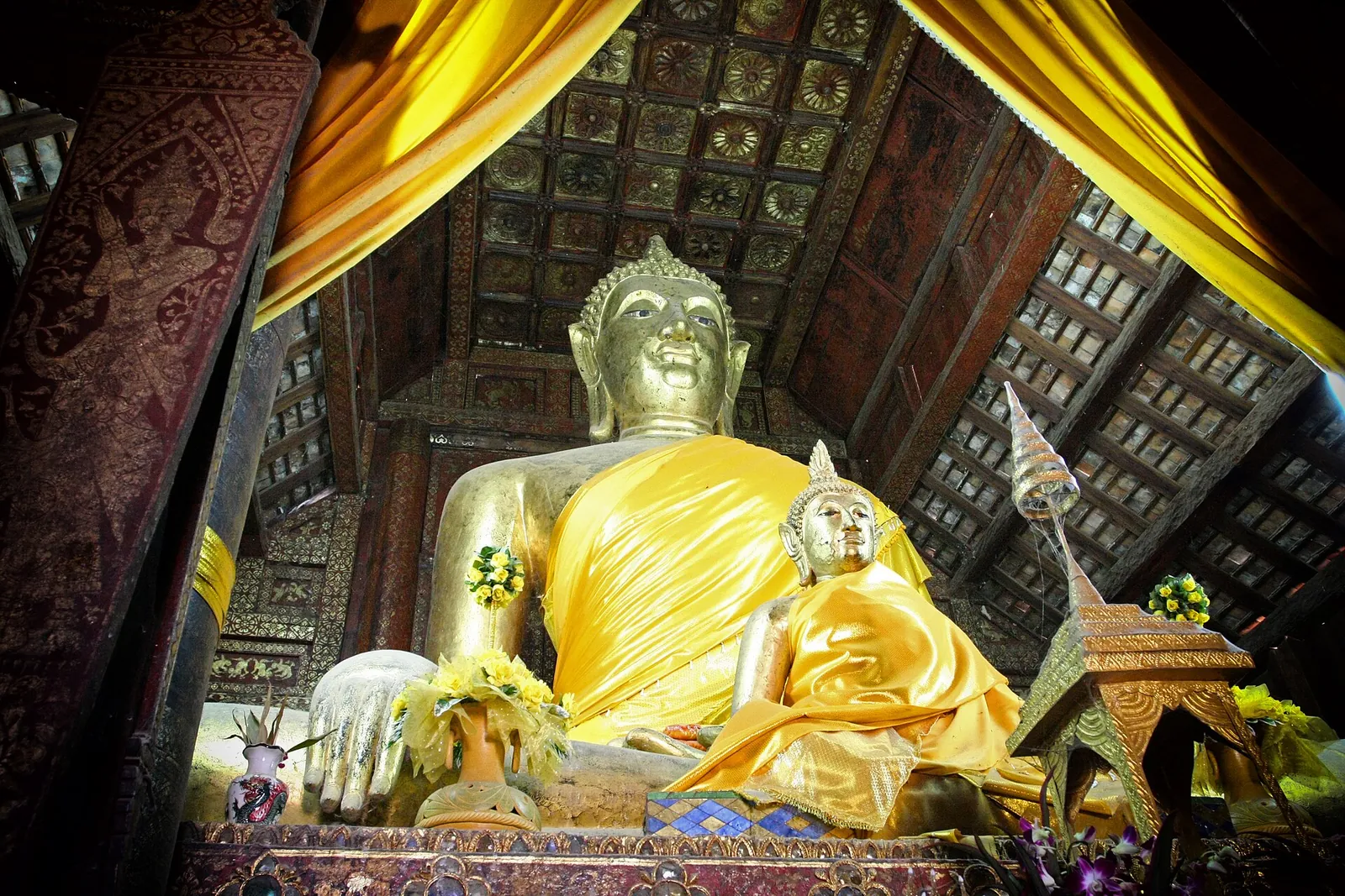 Ein vergoldeter sitzender Buddha mit gelbem Tuch in einer alten hölzernen Lanna-Halle