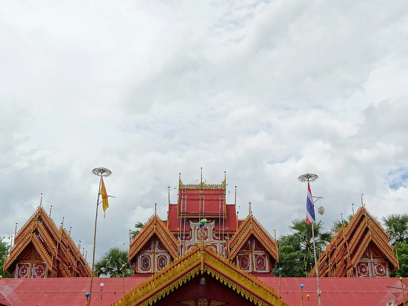 Die gestaffelten rot-goldenen Dächer des Wat Si Rong Mueang unter bewölktem Himmel