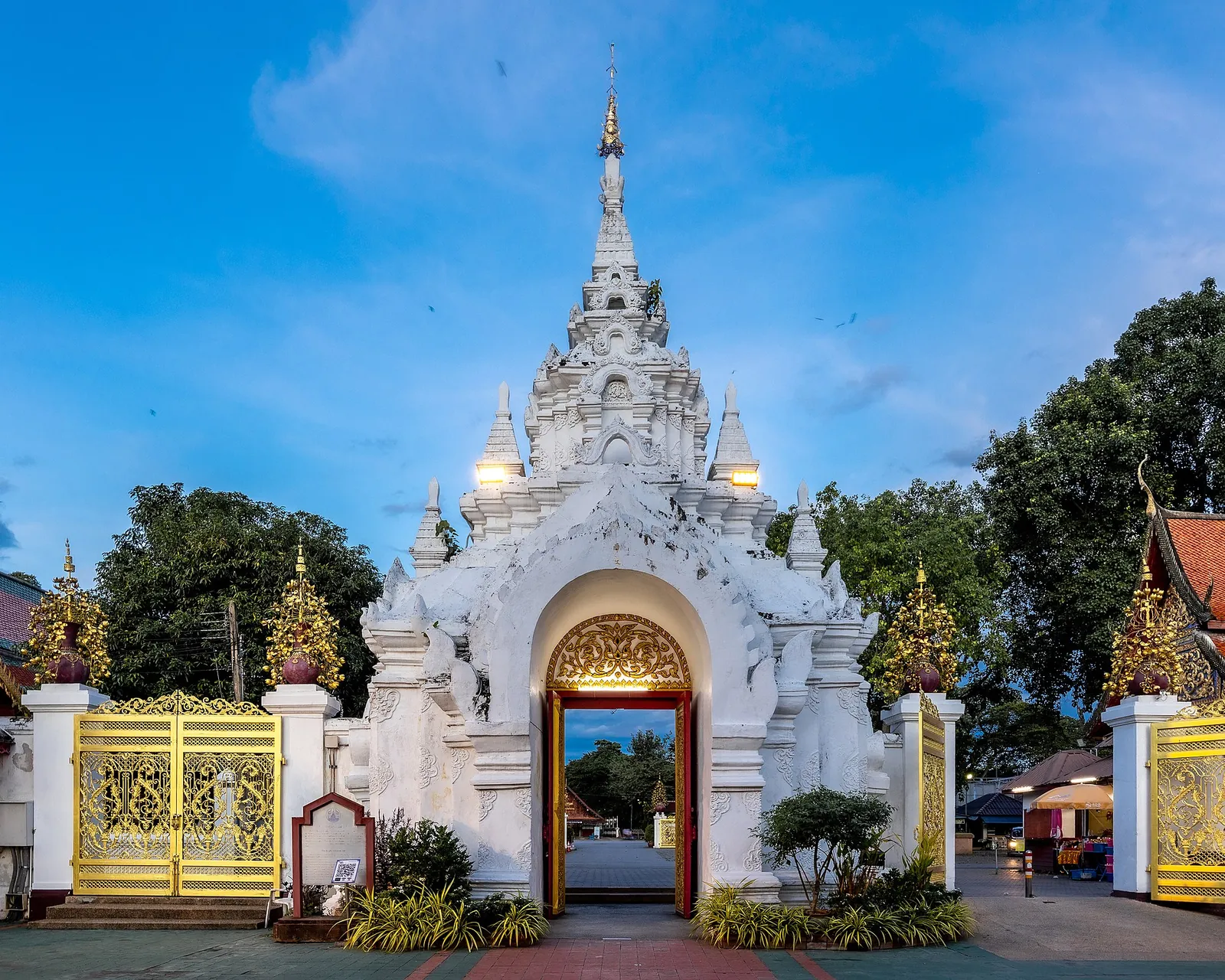 The white stucco gate of Wat Phra That Hariphunchai with a spire above the arch