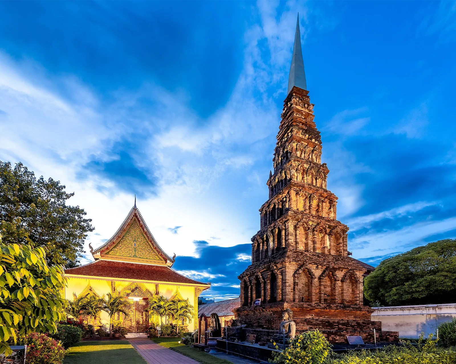 The stepped brick Suwan Chedi rising beside a golden hall at Wat Phra That Hariphunchai