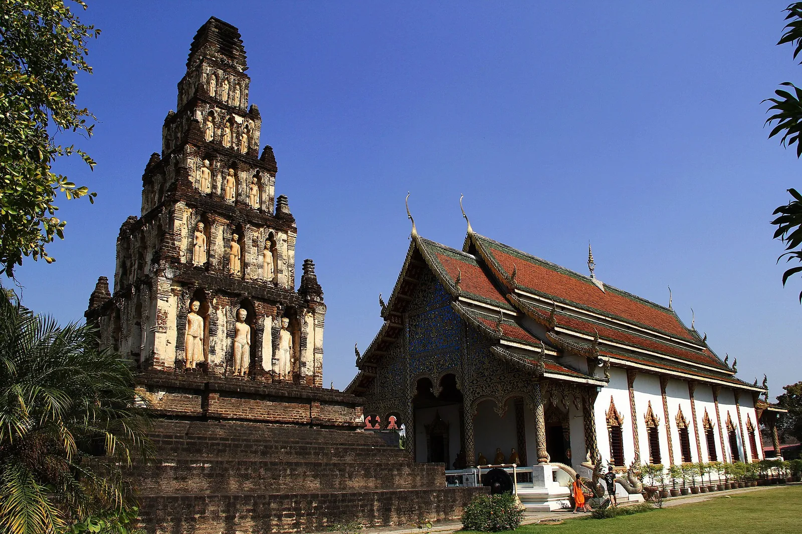 The stepped brick chedi of Wat Chamthewi with Buddha niches next to a white hall with a red roof