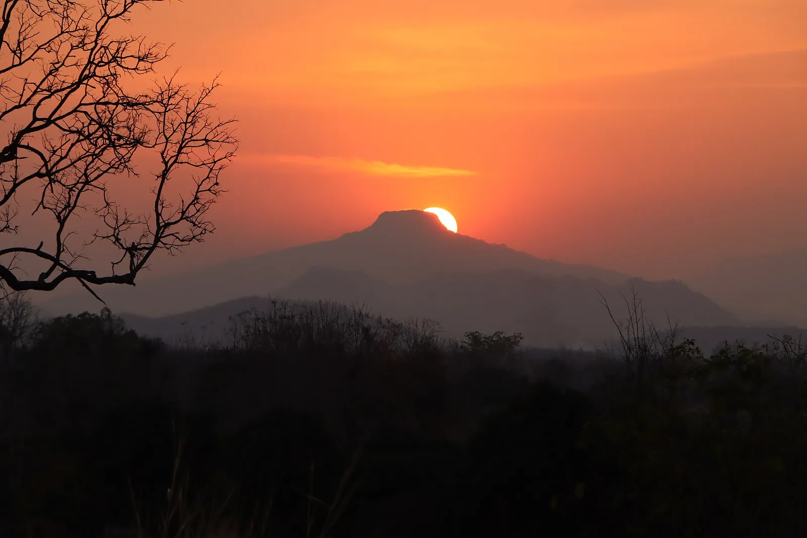 The sun setting behind the cone-shaped peak of Phu Ho seen from Phu Pa Po