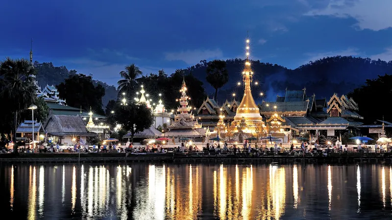 The lit Burmese-style chedis of Wat Chong Klang and Wat Chong Kham reflected in Nong Chong Kham lake at dusk