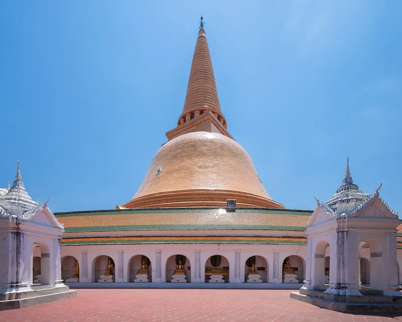 The orange-tiled dome and spire of Phra Pathom Chedi above white galleries on a clear day