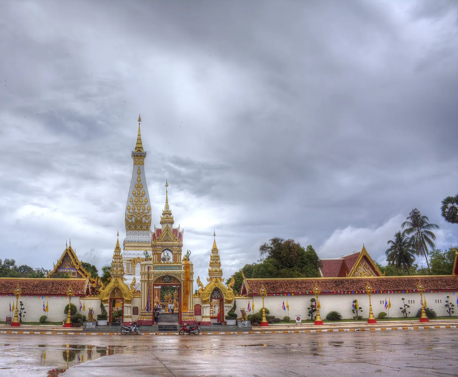 The tall white-and-gold stupa of Wat Phra That Phanom behind its gate under a dramatic sky