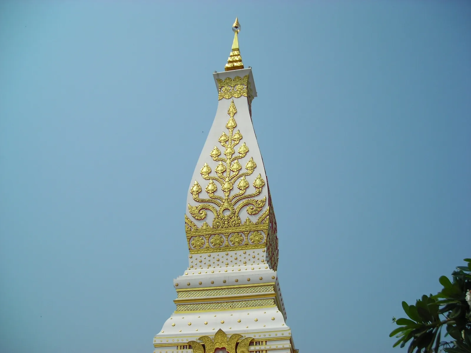 Close view of the gilded upper tiers of the That Phanom stupa against a blue sky
