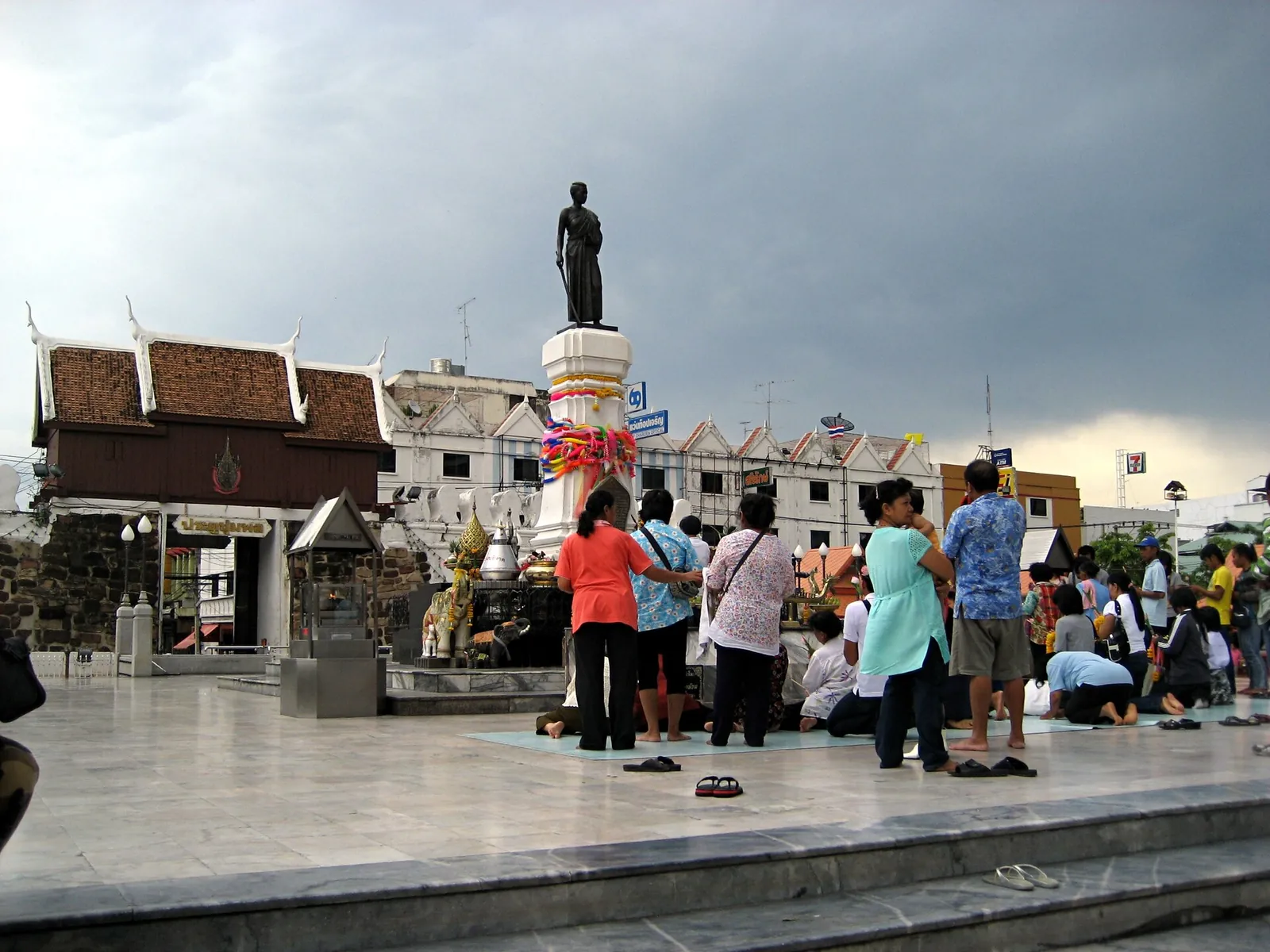 The bronze statue of Thao Suranari on a tall plinth with worshippers making offerings below