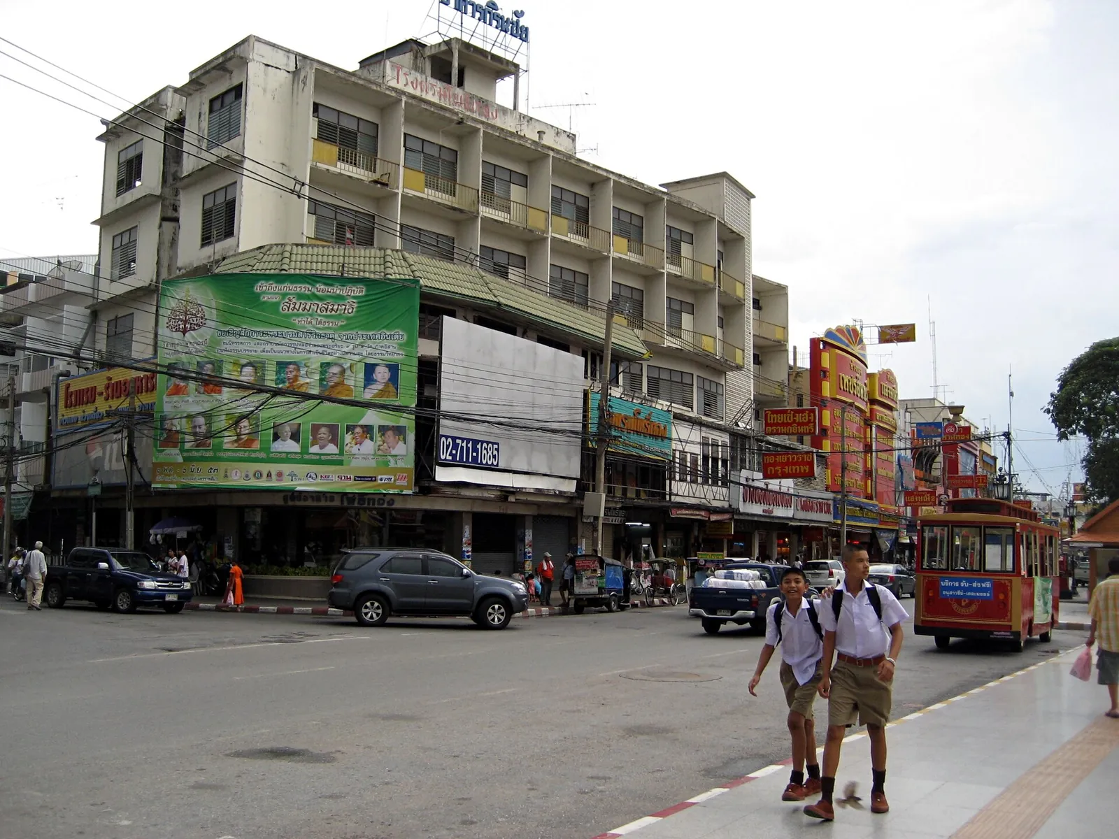 A busy street in downtown Korat with shophouses, a hotel and a red tour tram