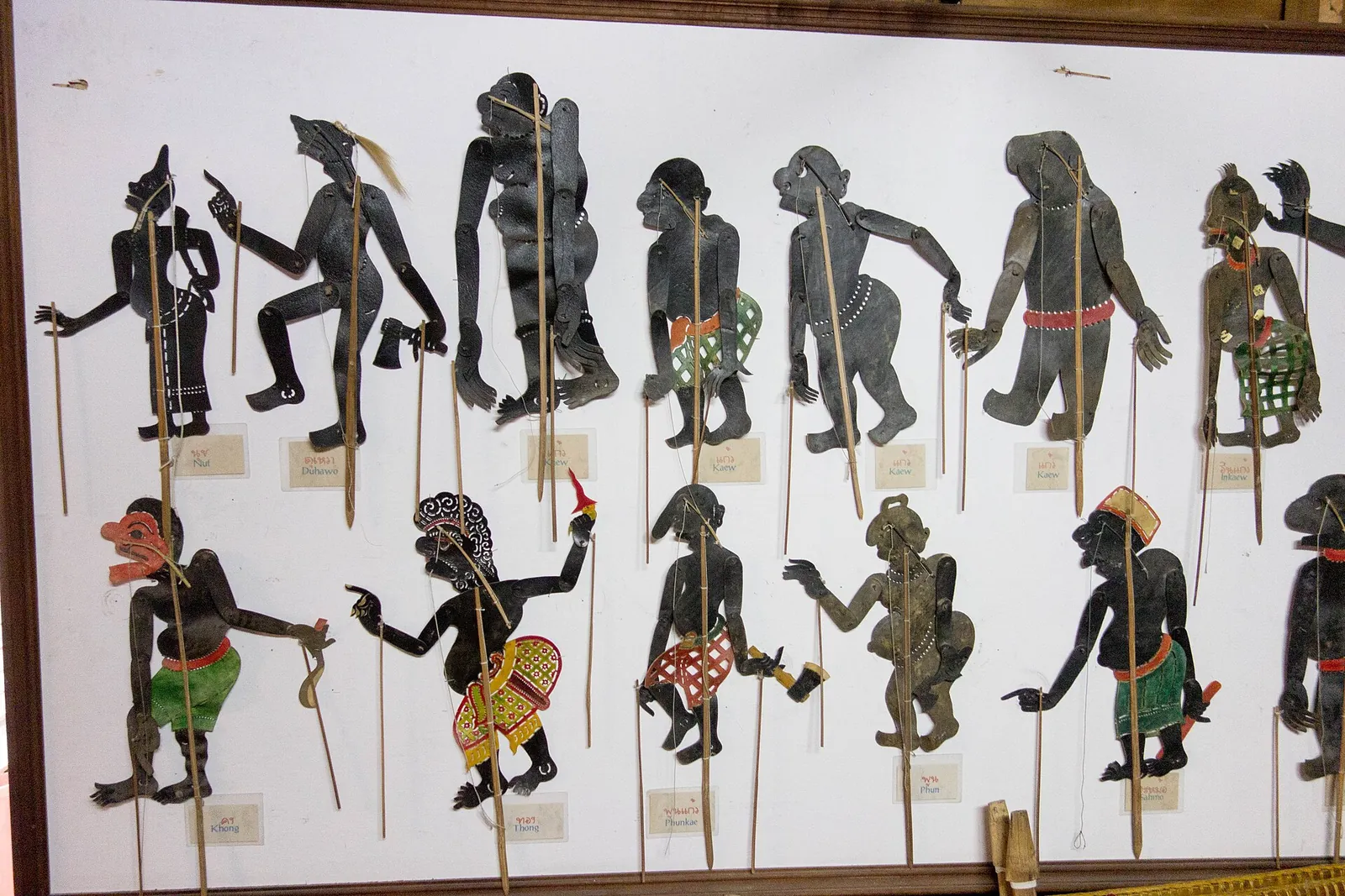 A row of cut leather shadow puppets of Nang Talung characters on a white wall