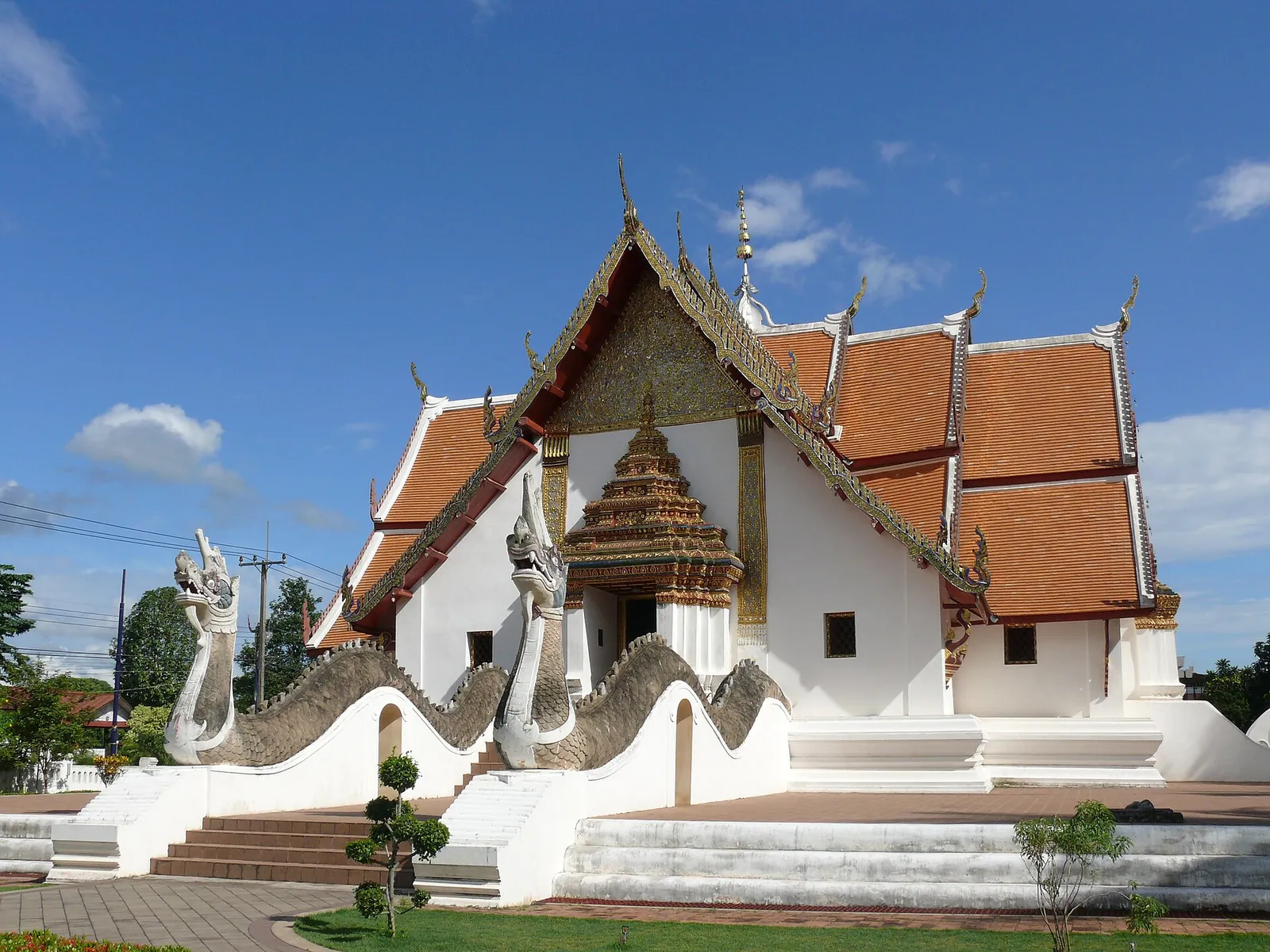 The white cross-shaped hall of Wat Phumin with naga balustrades and tiered orange roofs
